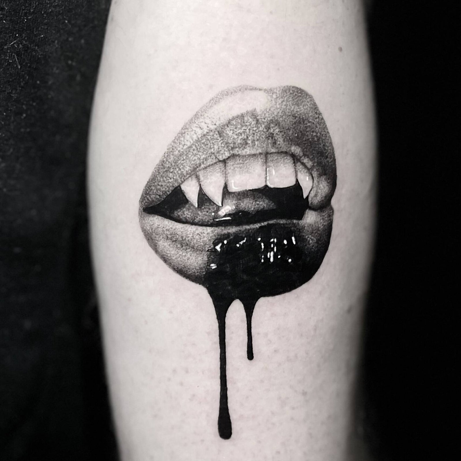 Tattoo of realistically shaded fanged lips with solid black ink dripping downward, on the leg.