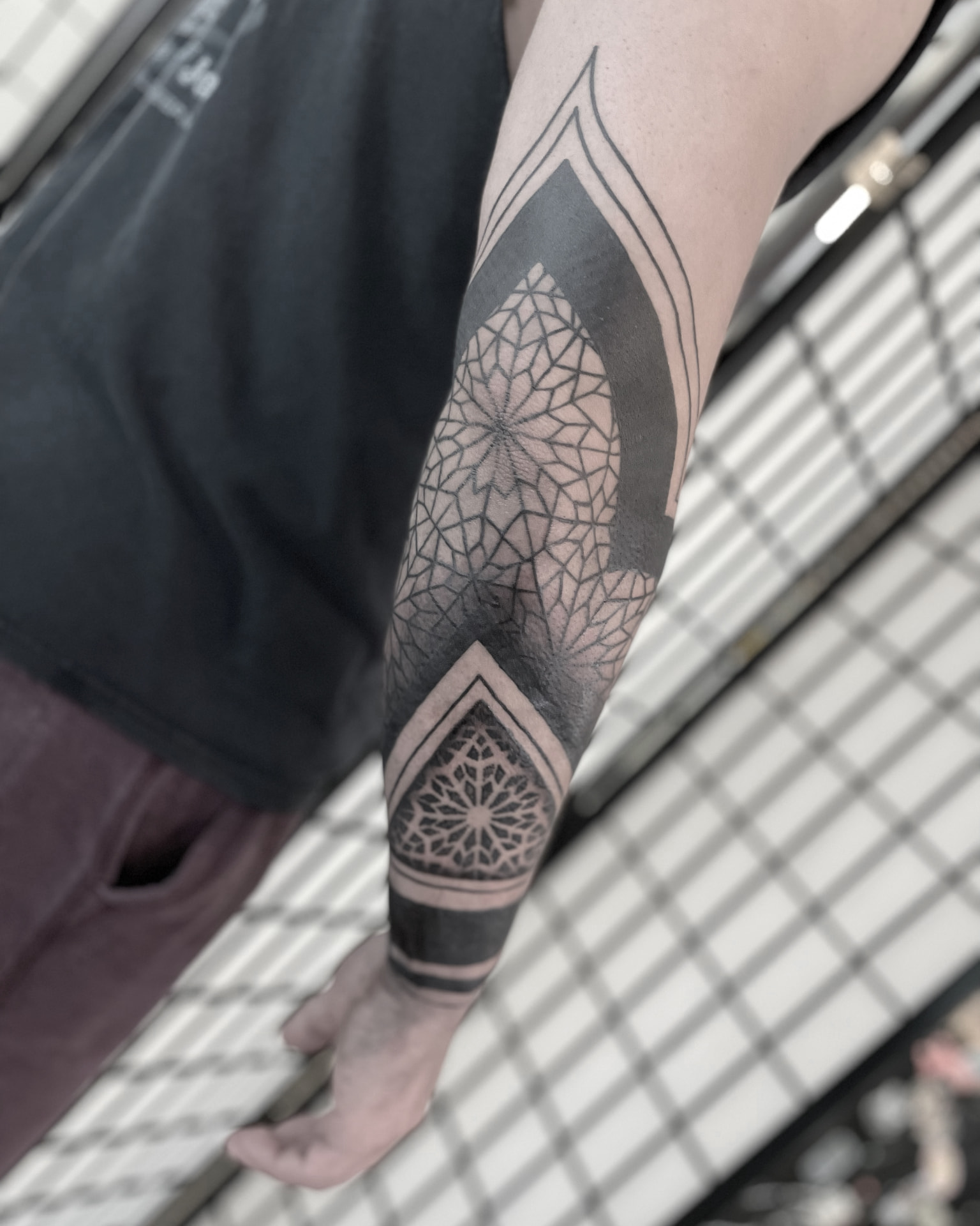Geometric blackwork tattoo with radial patterns and solid black panels around the elbow and forearm.