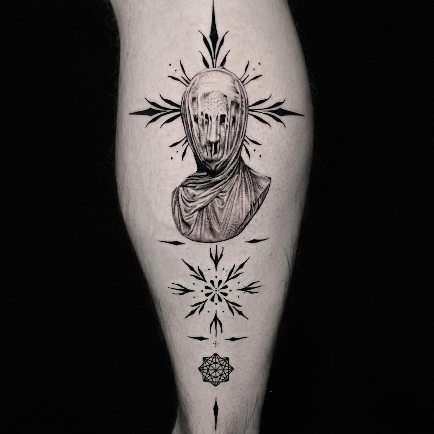 Black and grey tattoo of a hooded draped figure with thorn rays and ornamental motifs down the calf.