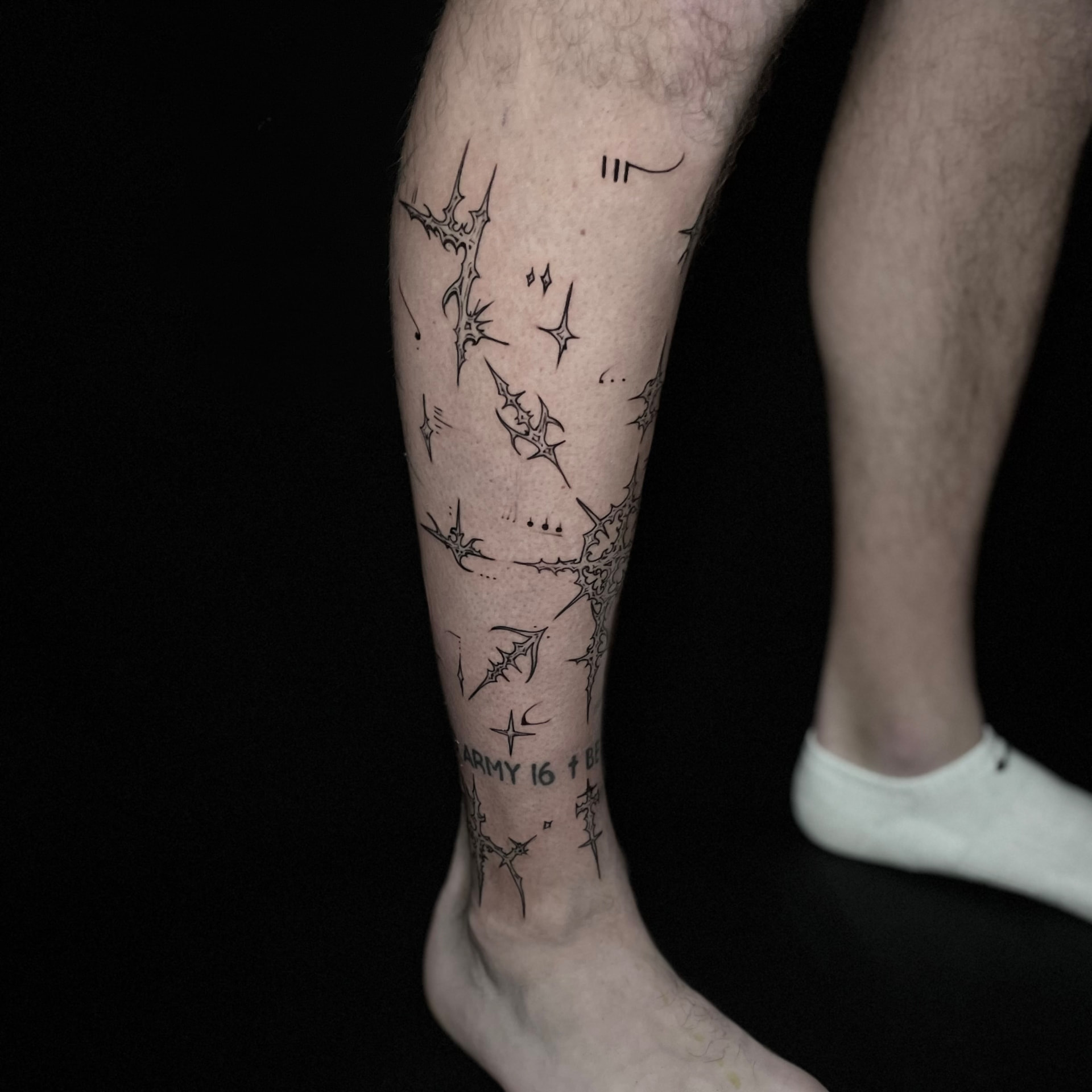 Fine black abstract sigil tattoo with stars and sharp linear forms across the calf.