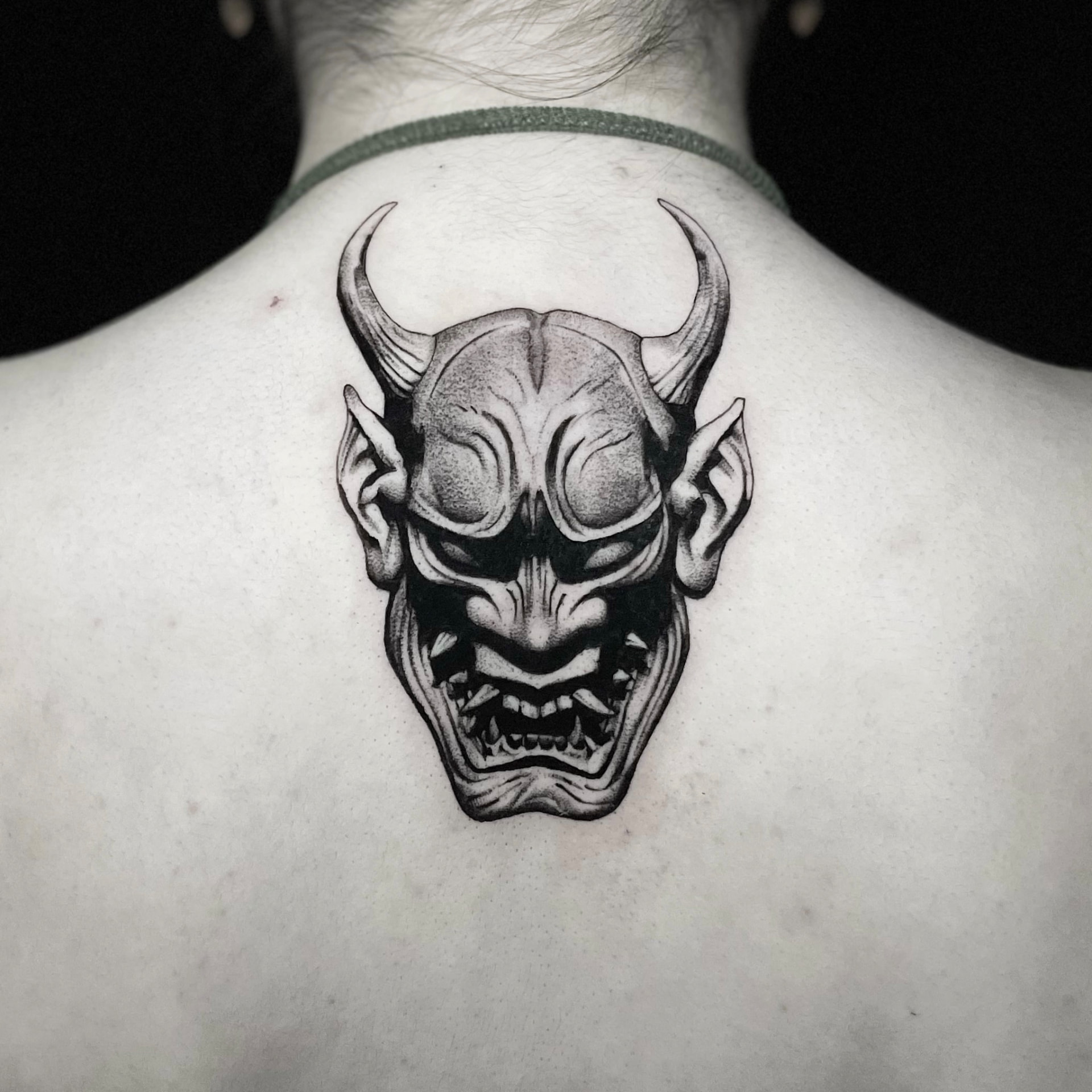 Black and grey hannya mask tattoo on the back of the neck and upper back.