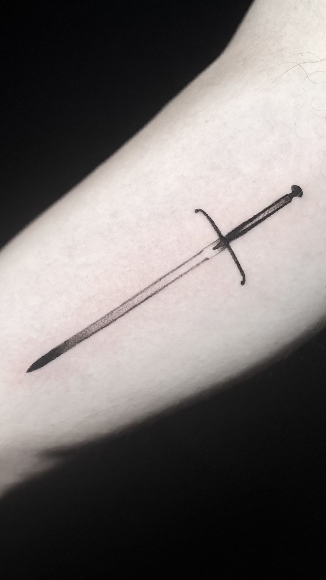 Fineline sword tattoo set diagonally on the forearm.