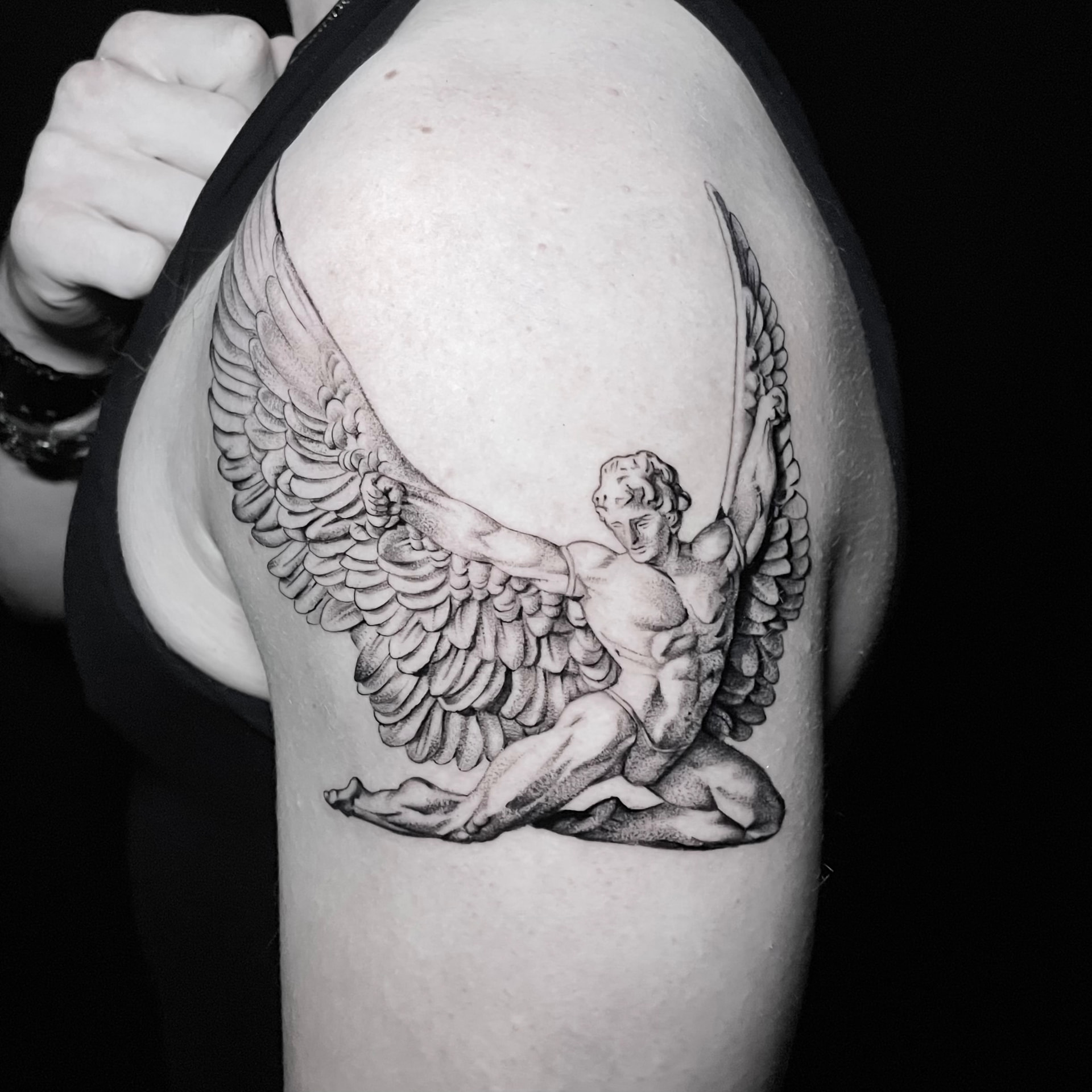 Black and grey tattoo of a winged Icarus figure on the shoulder.