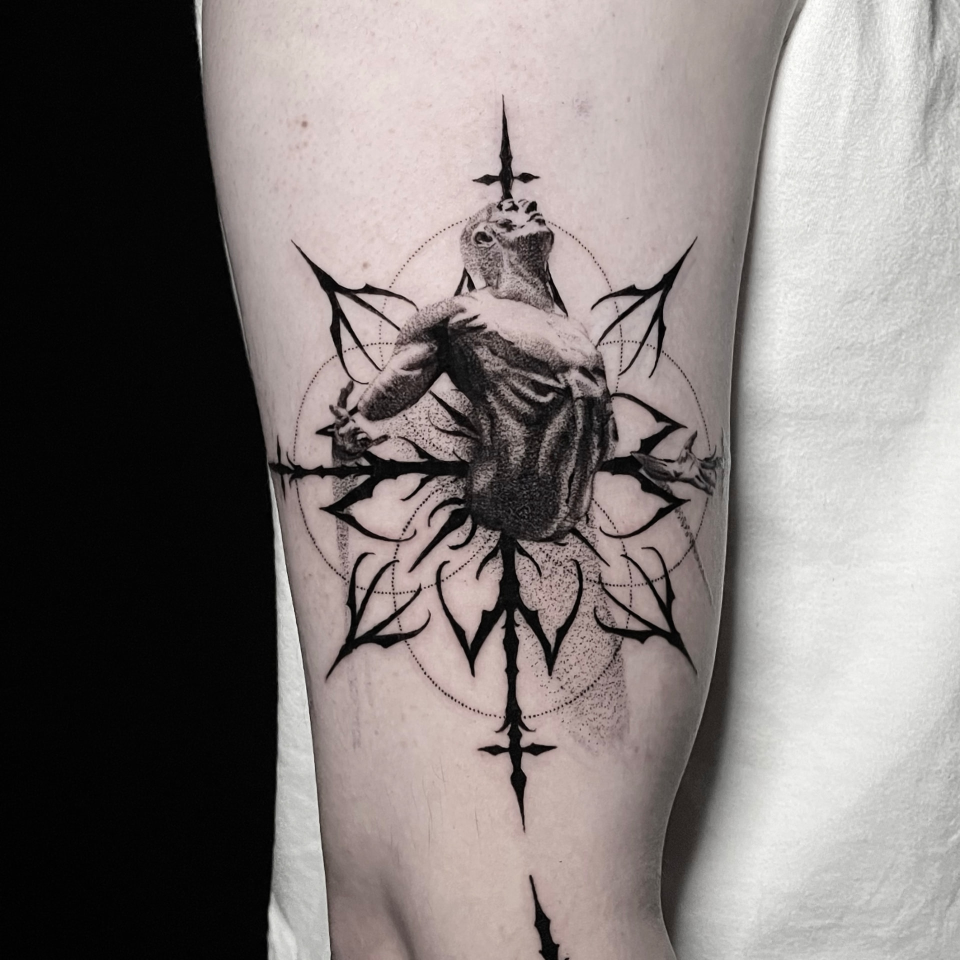 Black and grey tattoo of a figure inside a ring of thorns and dotted circles on the calf.