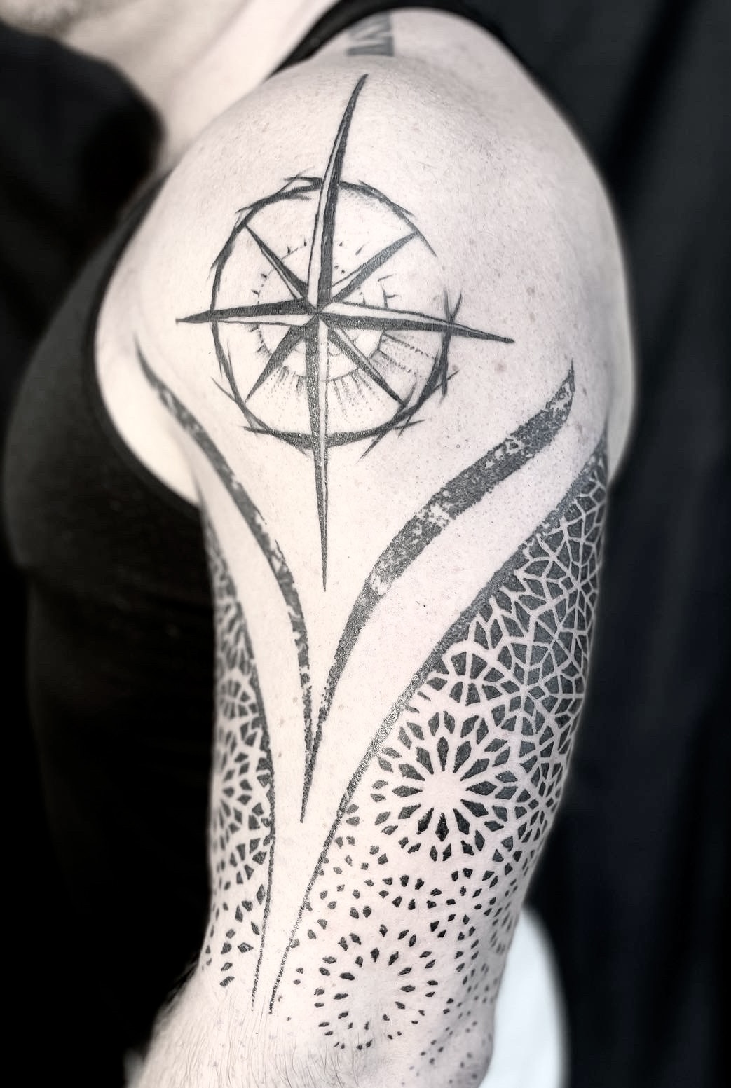 Blackwork compass star tattoo above geometric patterned bands on the shoulder and upper arm.