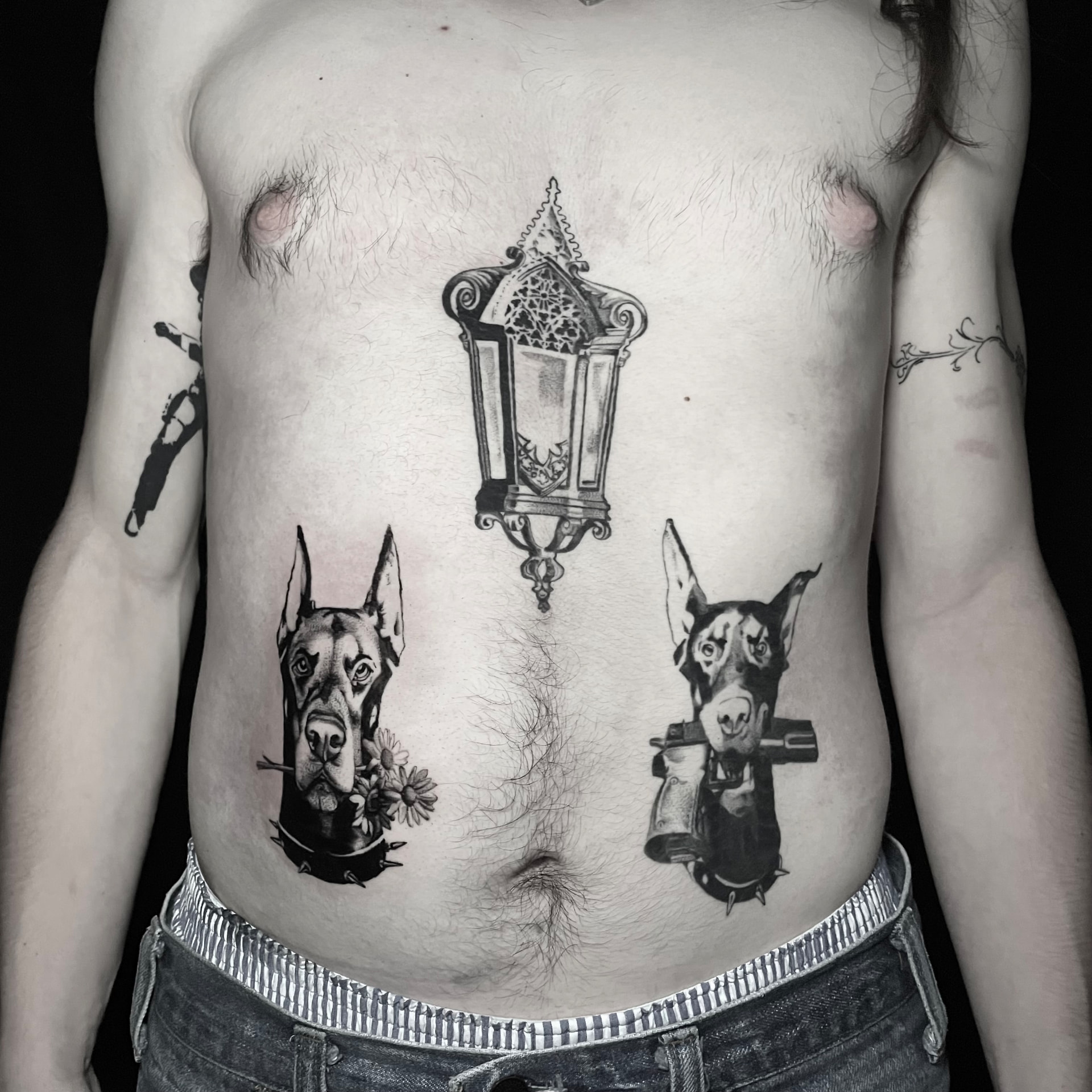 Black and grey torso tattoo of a gothic lantern on the sternum flanked by two doberman tattoos.