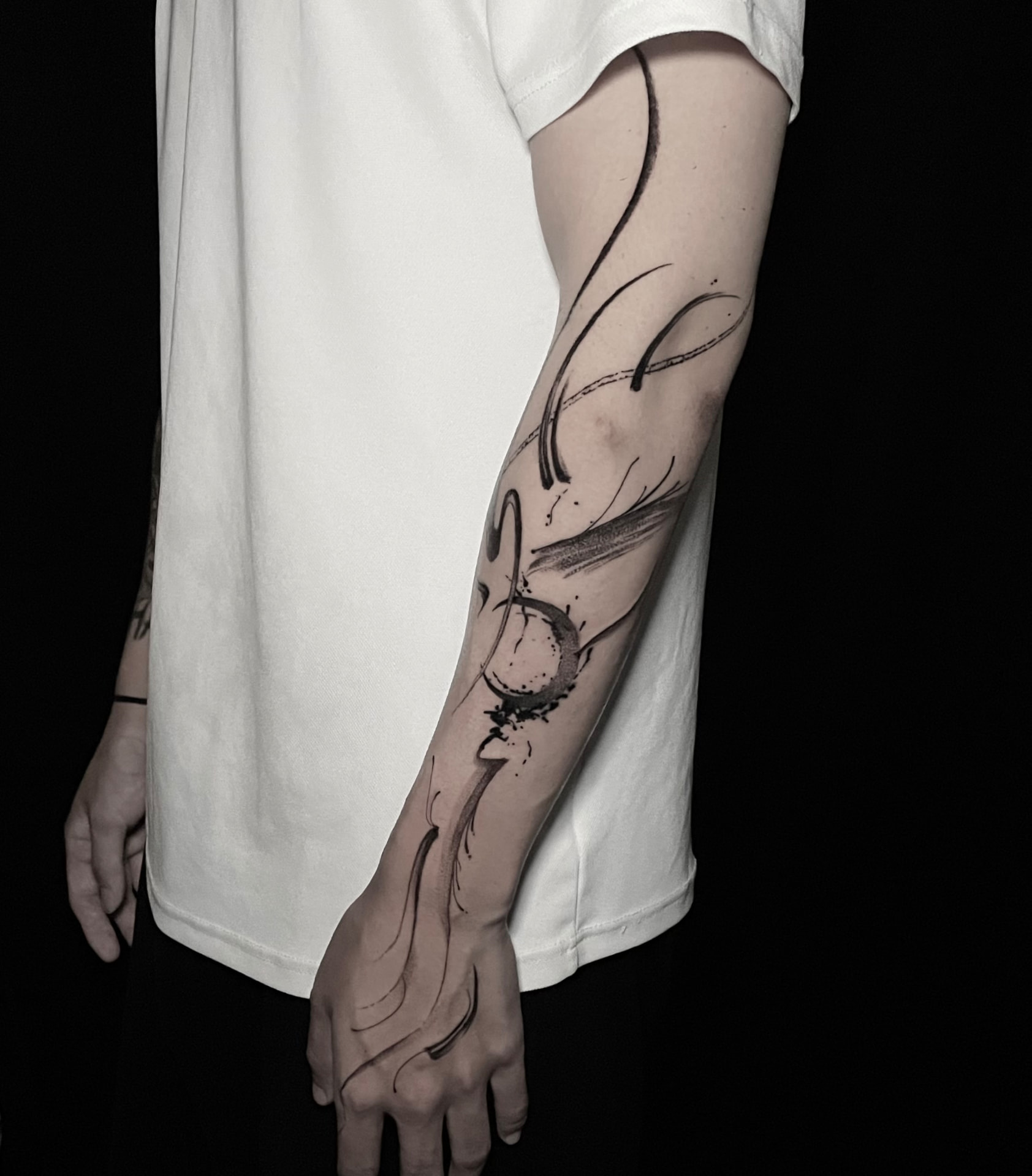 Abstract blackwork tattoo with sweeping curved lines and brush-like marks around the forearm and elbow.