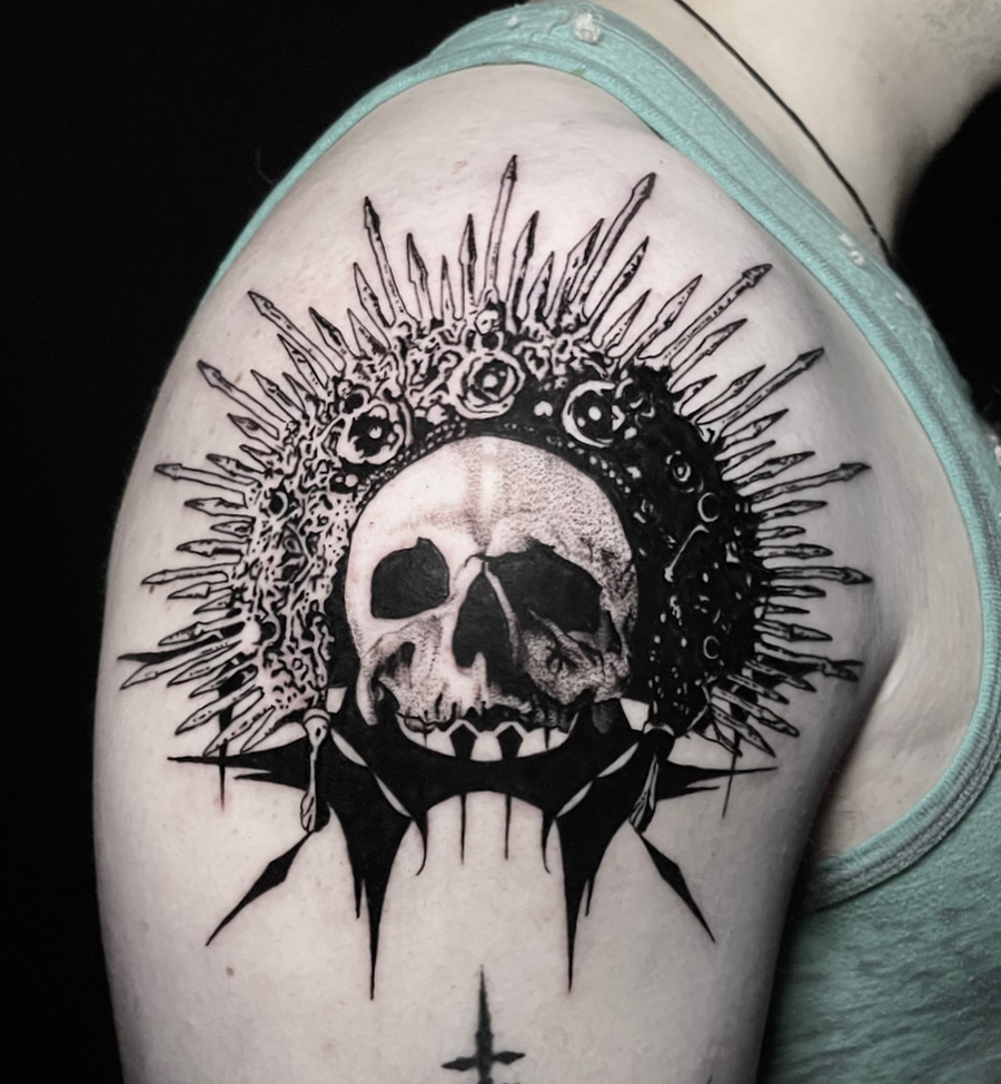Black and grey skull tattoo with an ornate spiked crown on the shoulder.