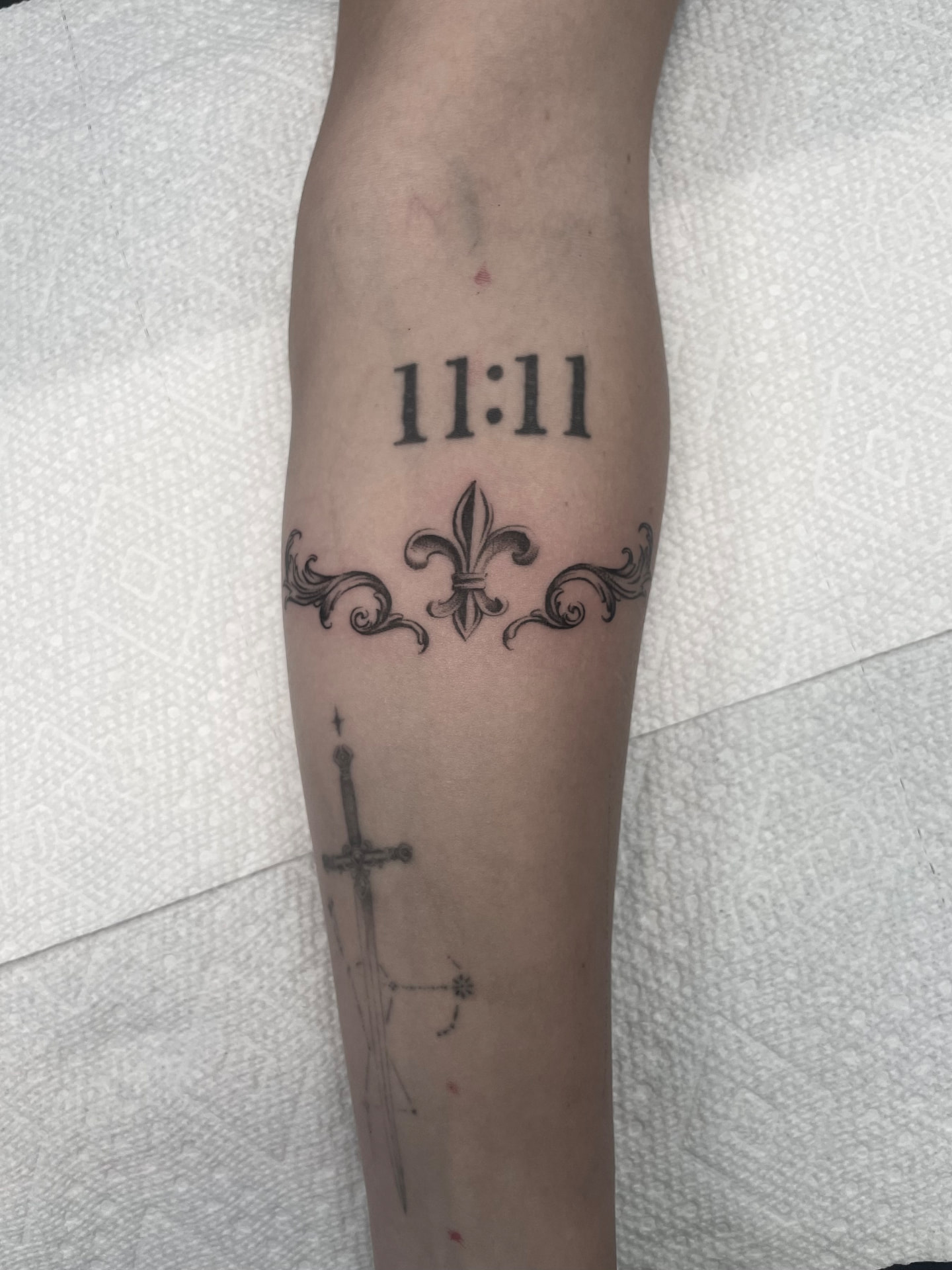 Fineline fleur-de-lis band with scrollwork and the numerals 11:11 on the forearm.
