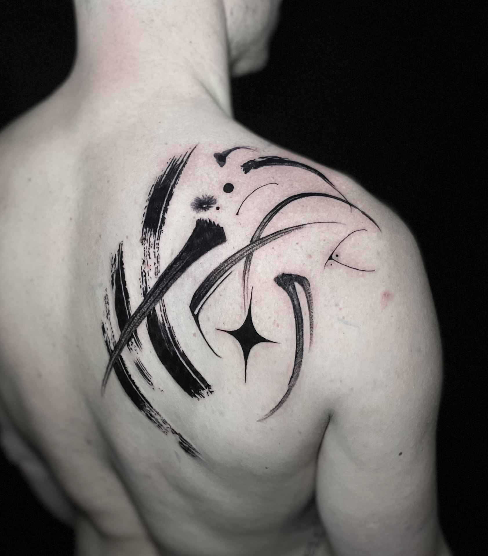 Abstract blackwork tattoo with curved brush strokes and fine graphic marks on the shoulder blade.