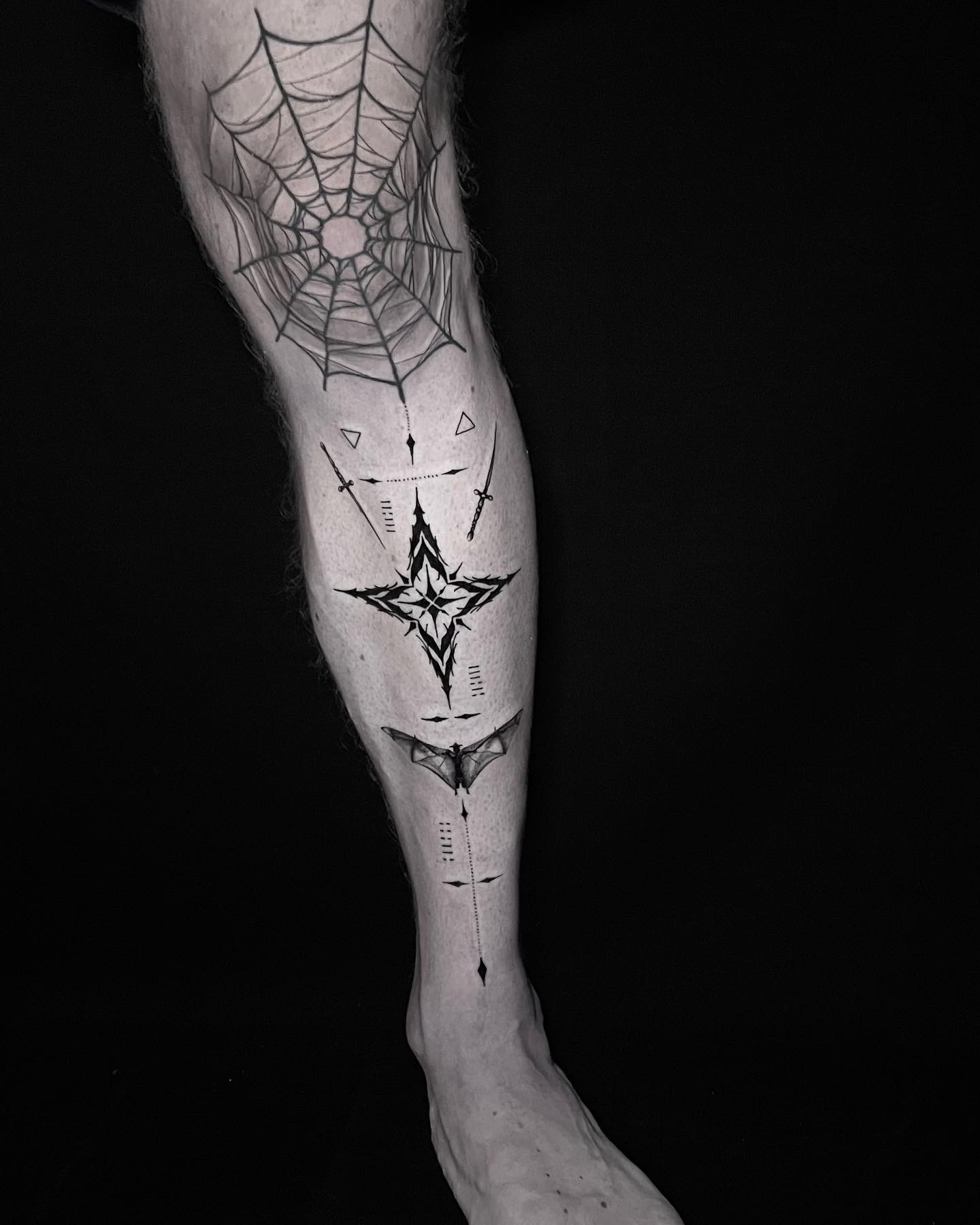 Blackwork spiderweb tattoo wrapping a calf with an ornamental star, daggers and geometric details down the leg.