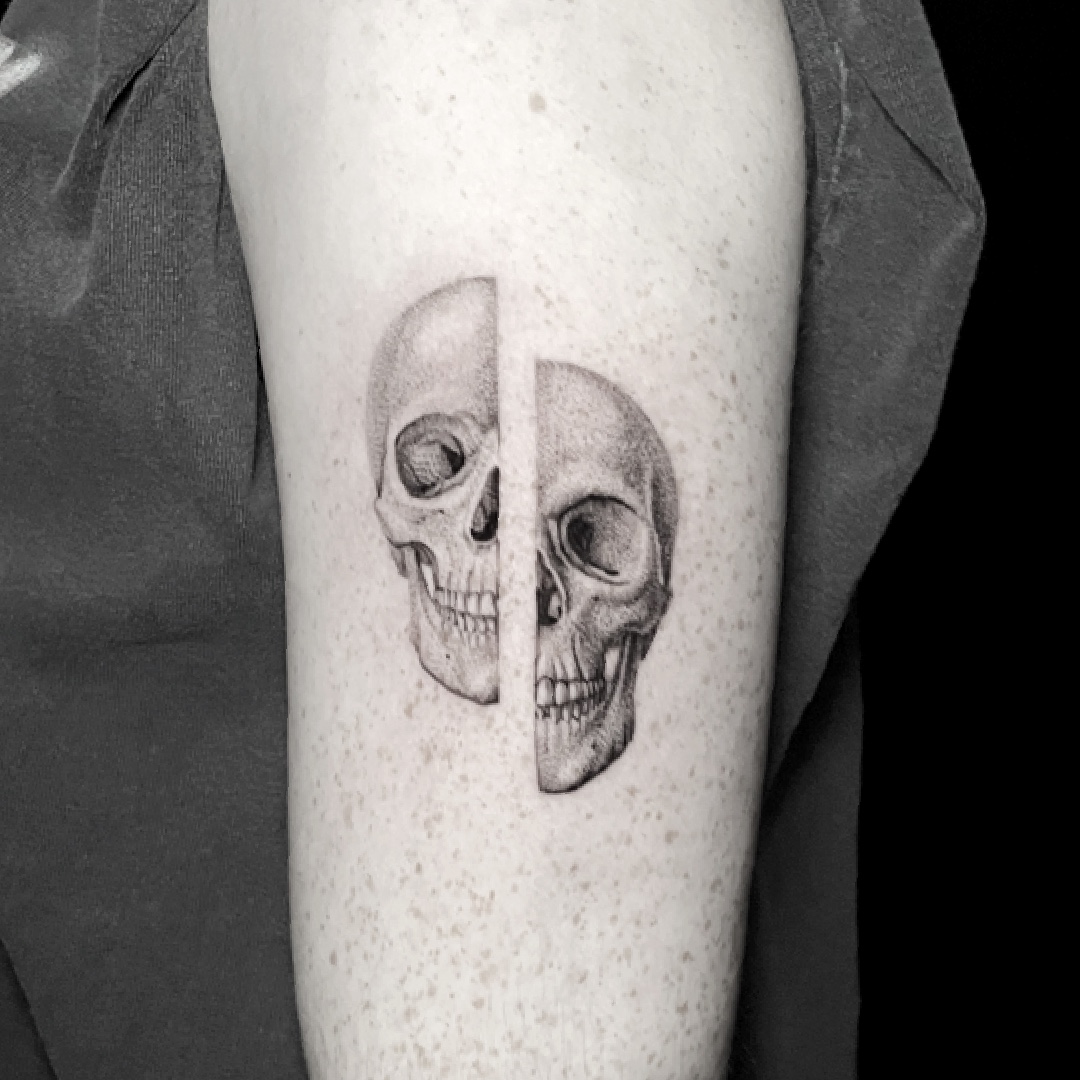 Black and grey tattoo of two split skull halves on the thigh.