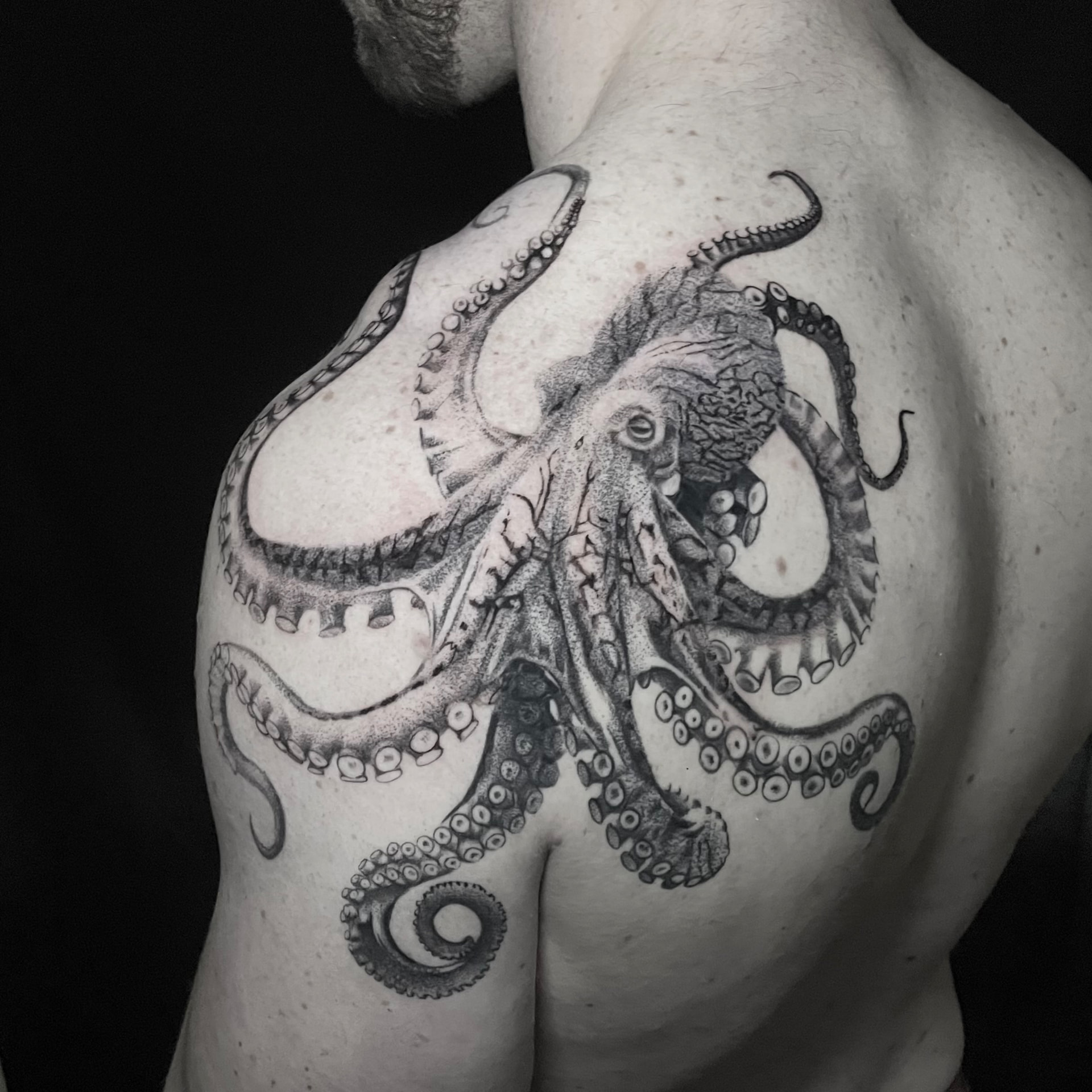 Large black and grey octopus tattoo wrapping over the shoulder and upper arm.