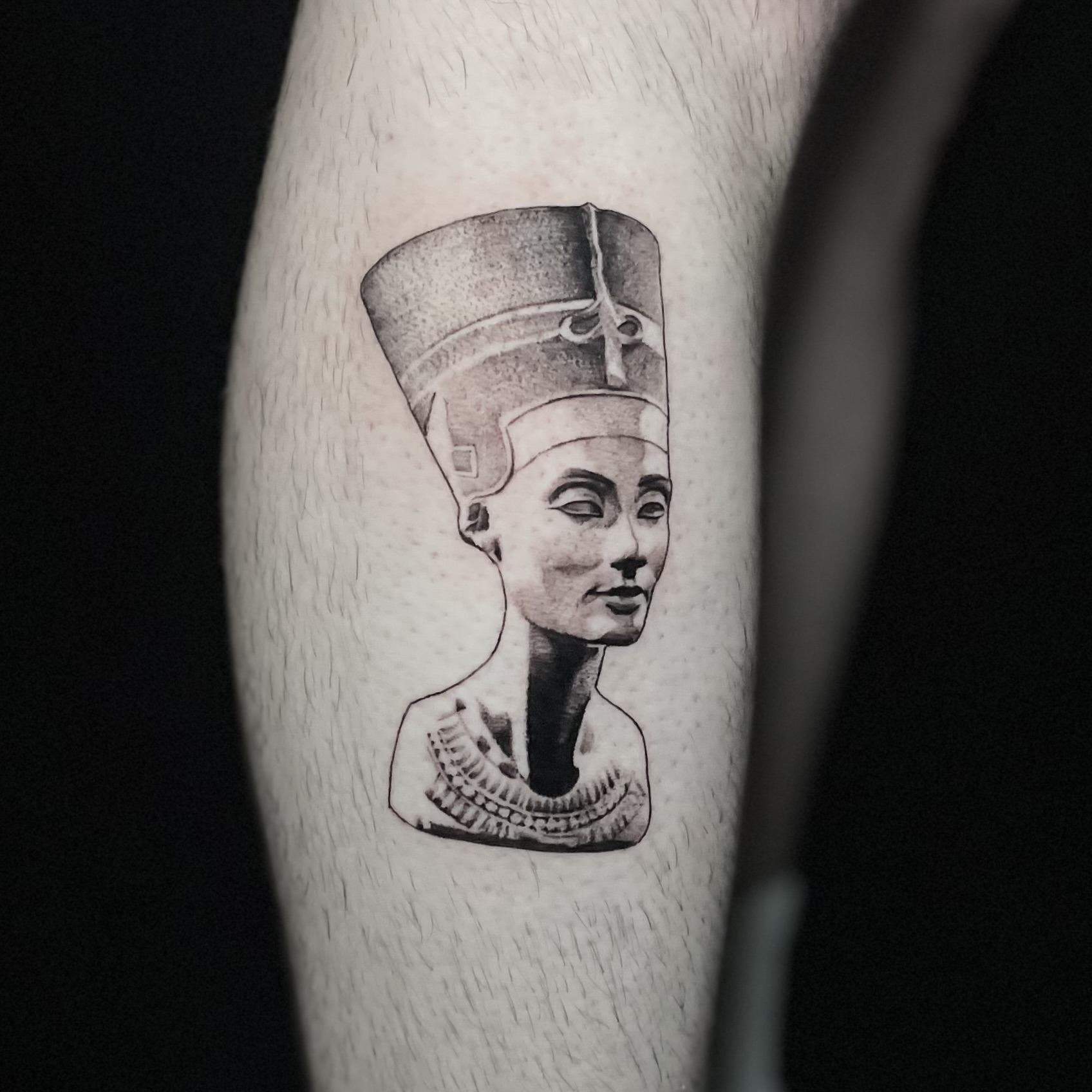 Black and grey stippled tattoo of the Nefertiti bust on the calf.