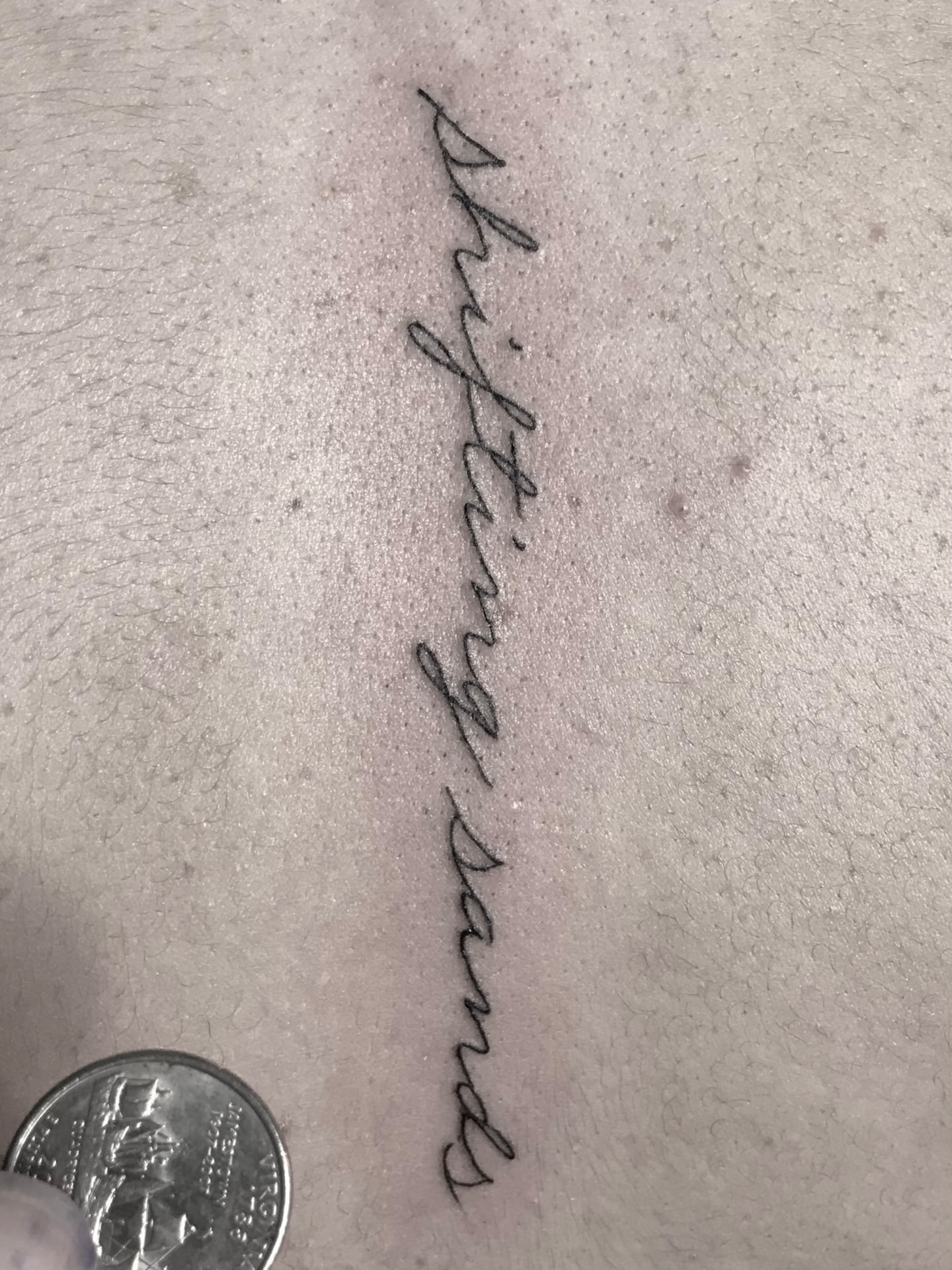 Close detail of a fine line script tattoo reading shifting sands.