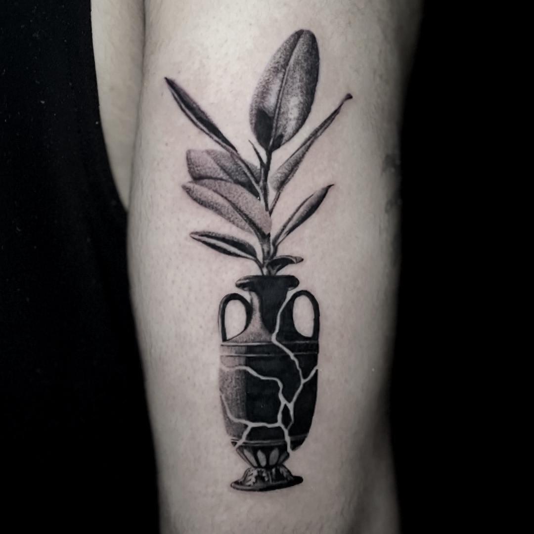 Black and grey tattoo of a cracked amphora with leafy branches on the forearm.