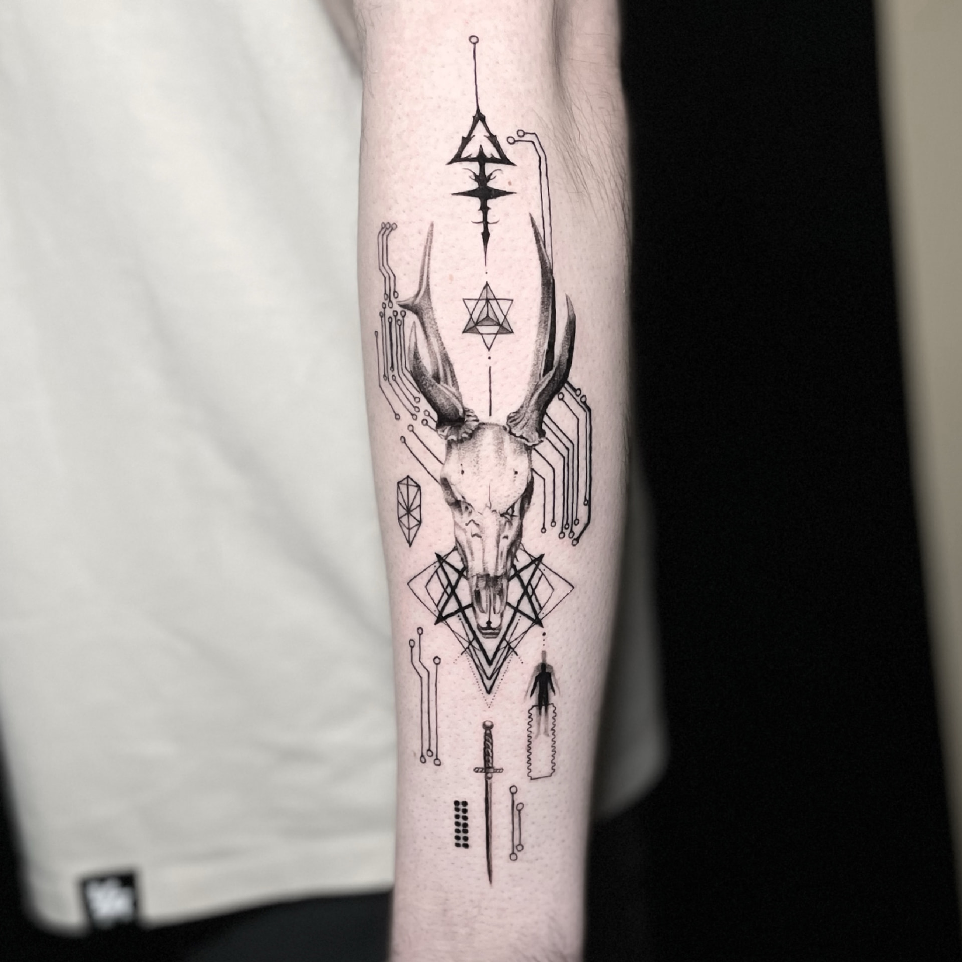 Black and grey deer skull tattoo with geometric and circuit-like ornament on the inner forearm.