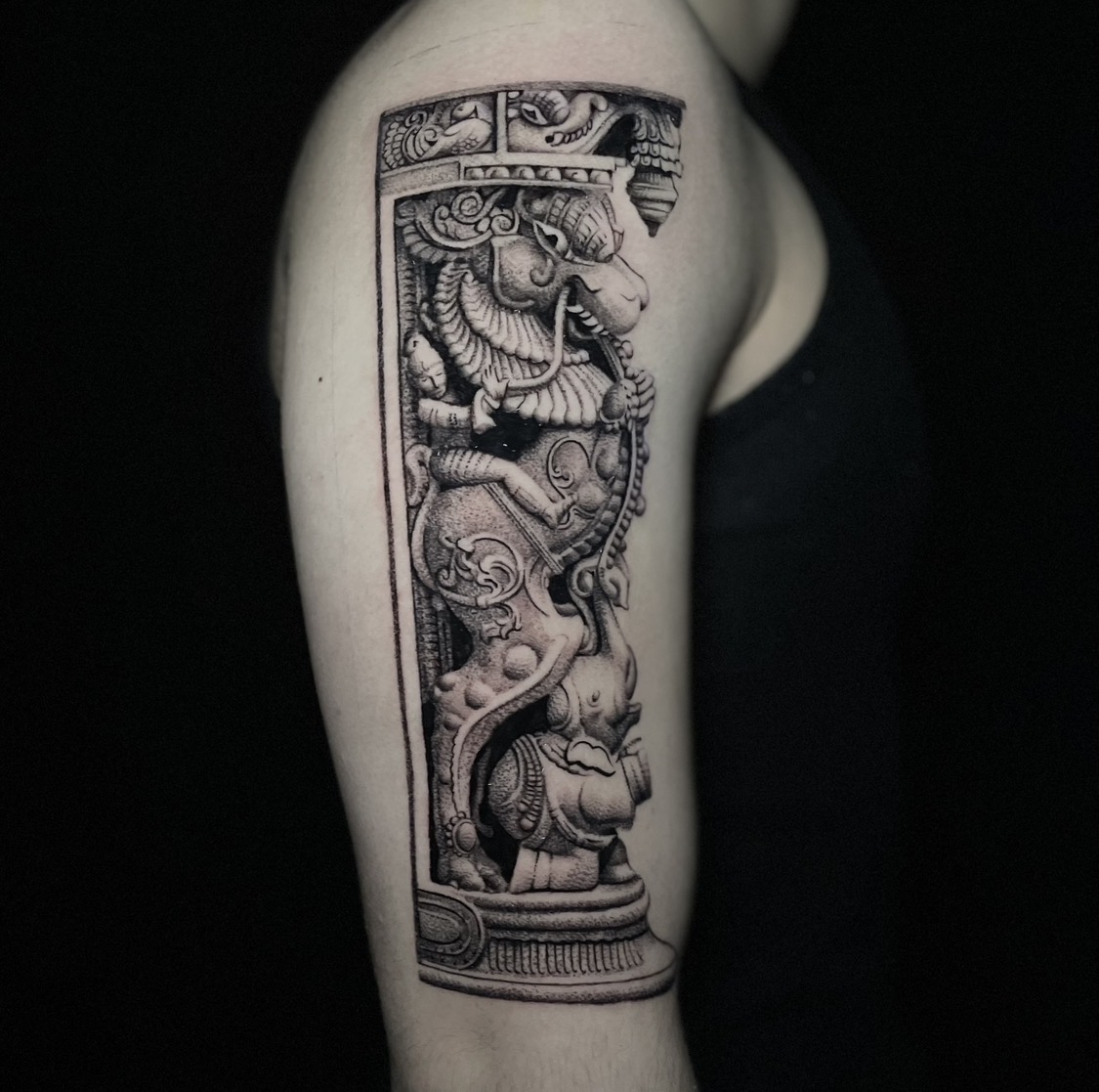 Black and grey tattoo of a carved South Indian temple pillar with a mythical yali lion on the upper arm.