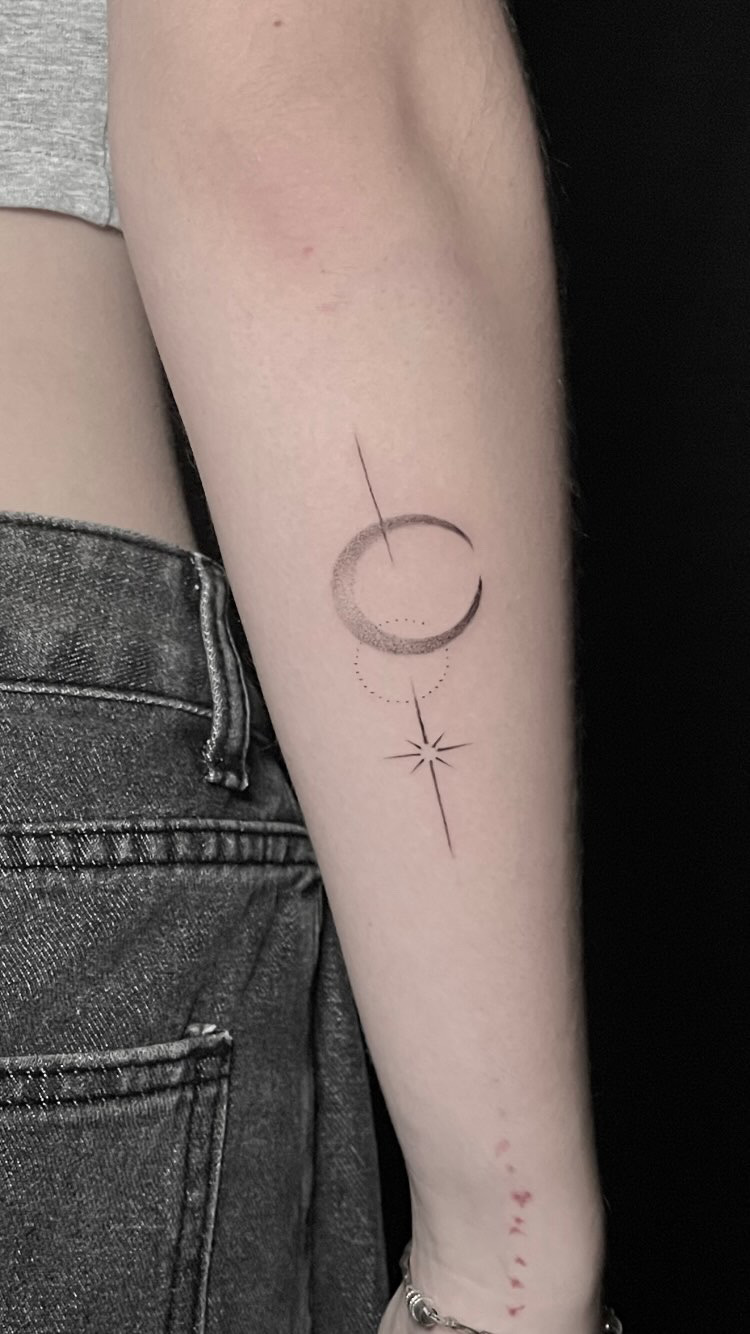 Fine line crescent moon and eight-point star tattoo on the forearm.