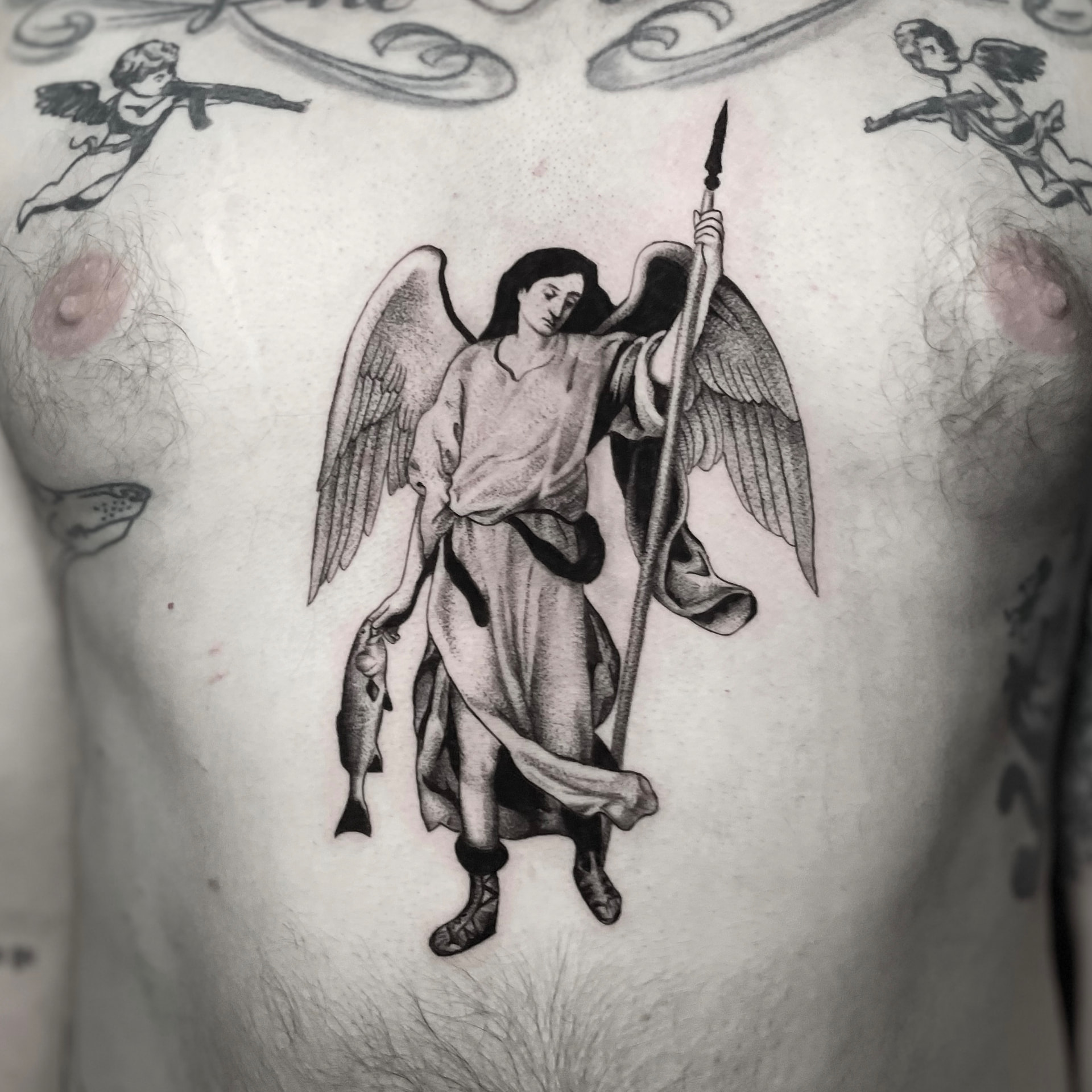 Black and grey chest tattoo of an archangel holding a spear and a fish, surrounded by small cherubs.