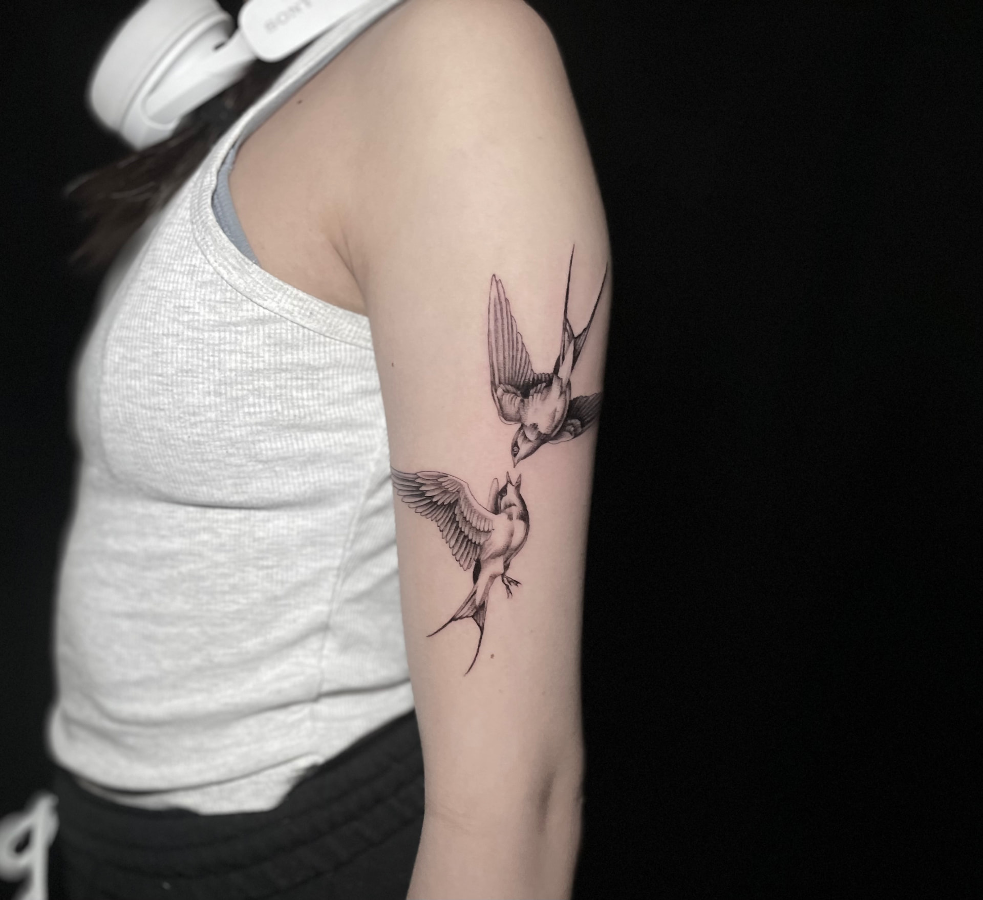 Two fine line swallow tattoos meeting in flight on the upper arm.